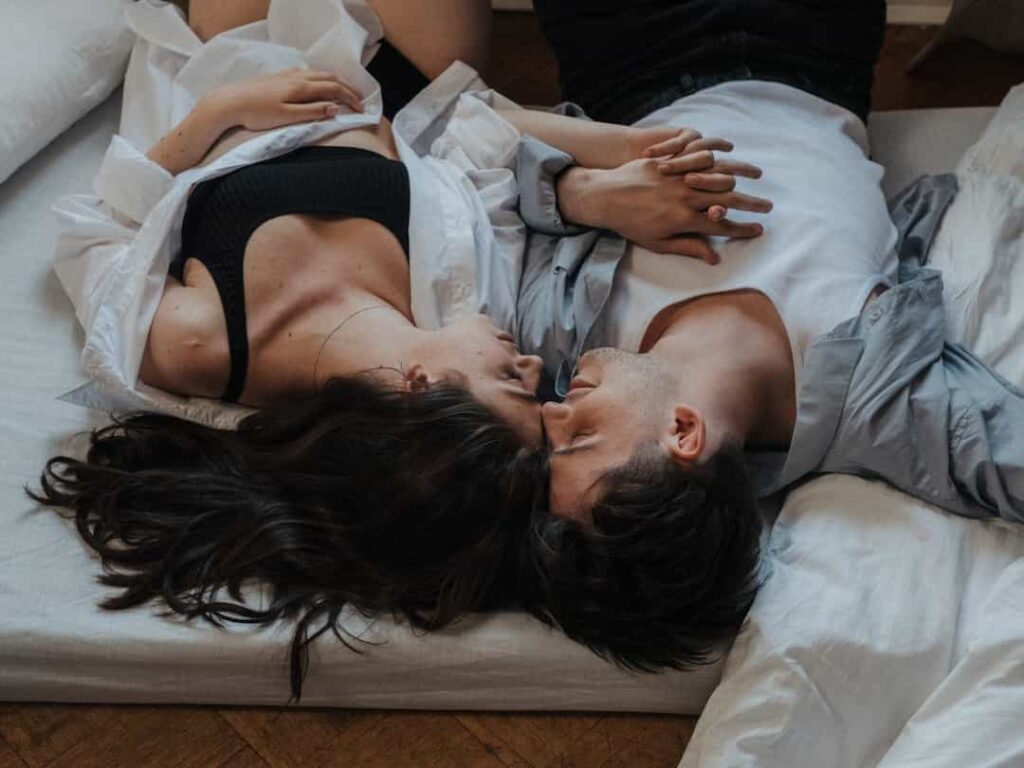 An image of couple holding hand and looking into each others' eyes on a floor mattress