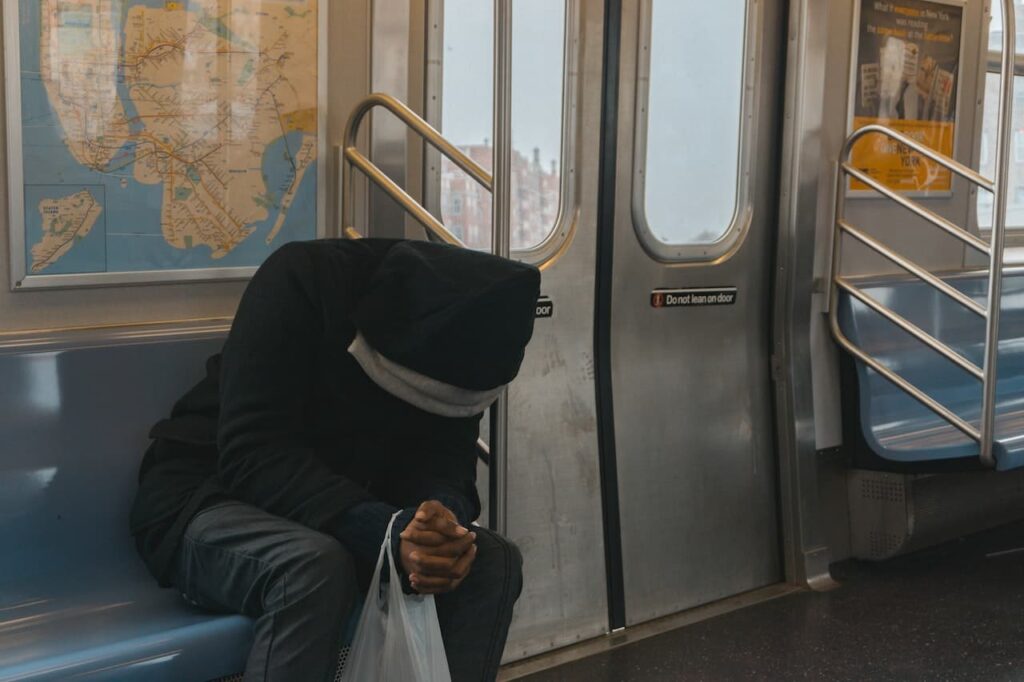 A man with a black hoodie praying on the subway. Photo by Steven Arenas Via Pexel